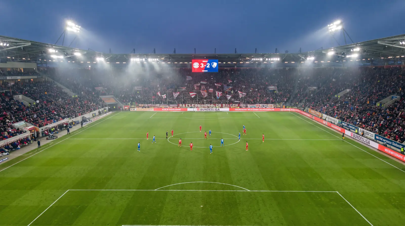 Terrain de football allemand vu de haut avec un tableau d'affichage indiquant un score de 3-2 en Bundesliga